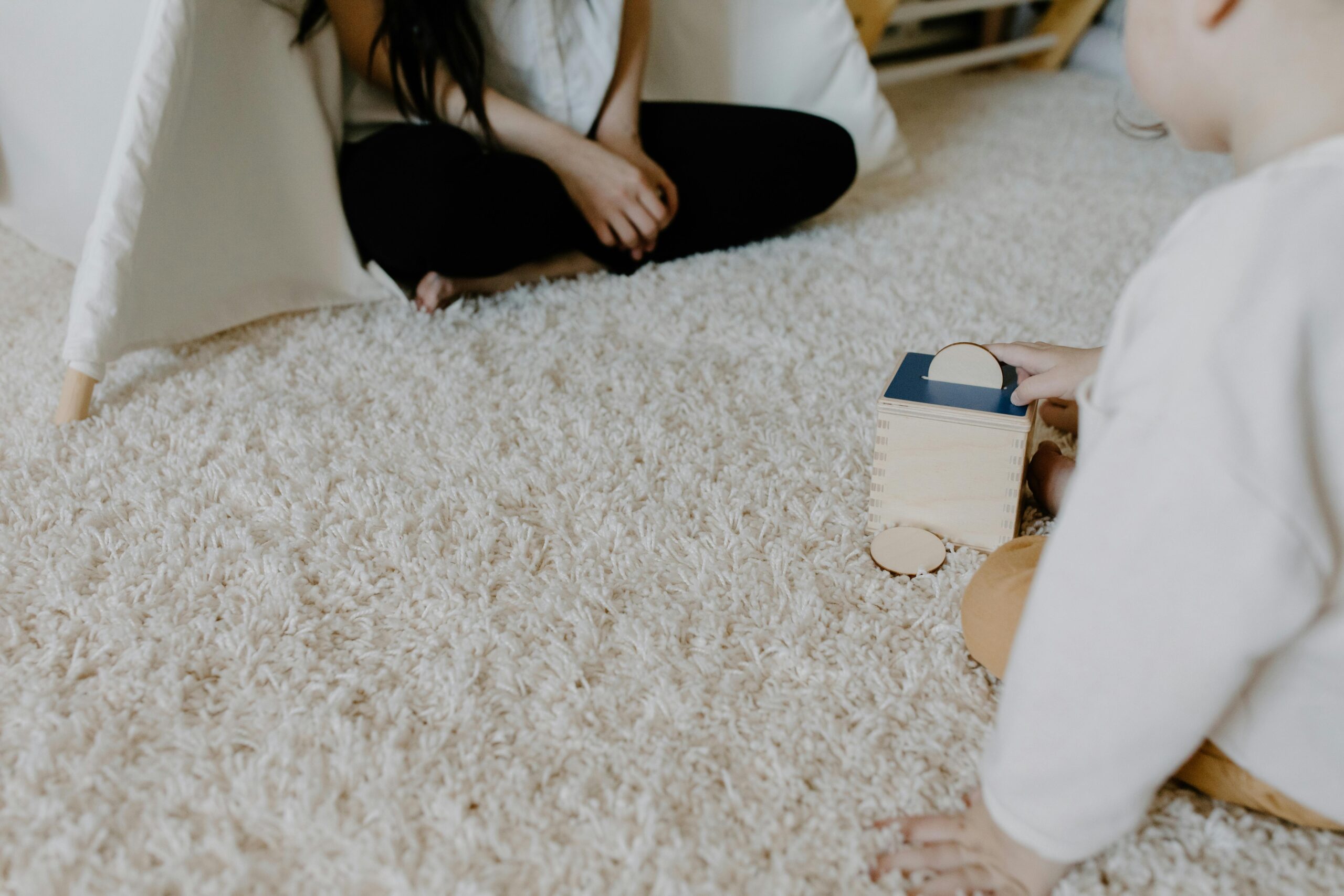 A child plays with a wooden block toy on a cozy carpet indoors, creating a warm family moment.
