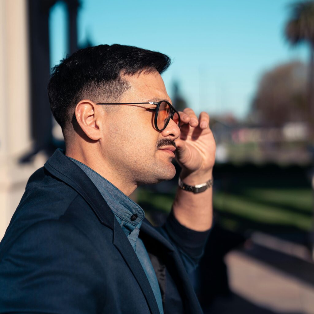 Profile of a stylish man wearing sunglasses in an outdoor setting, enjoying a bright day.